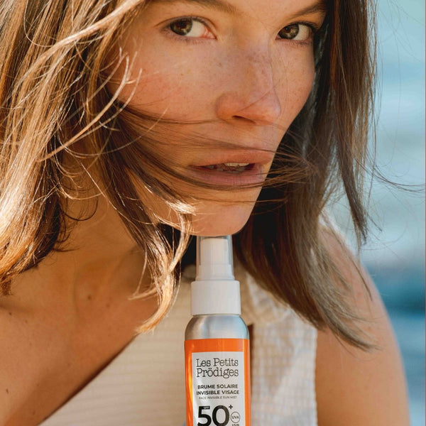 Femme au soleil tenant la Brume Solaire Invisible Visage SPF 50+