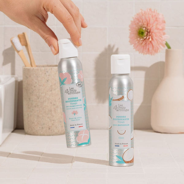 Main saisissant la Poudre Nettoyante Visage Fleur de Coton sur une étagère de salle de bain