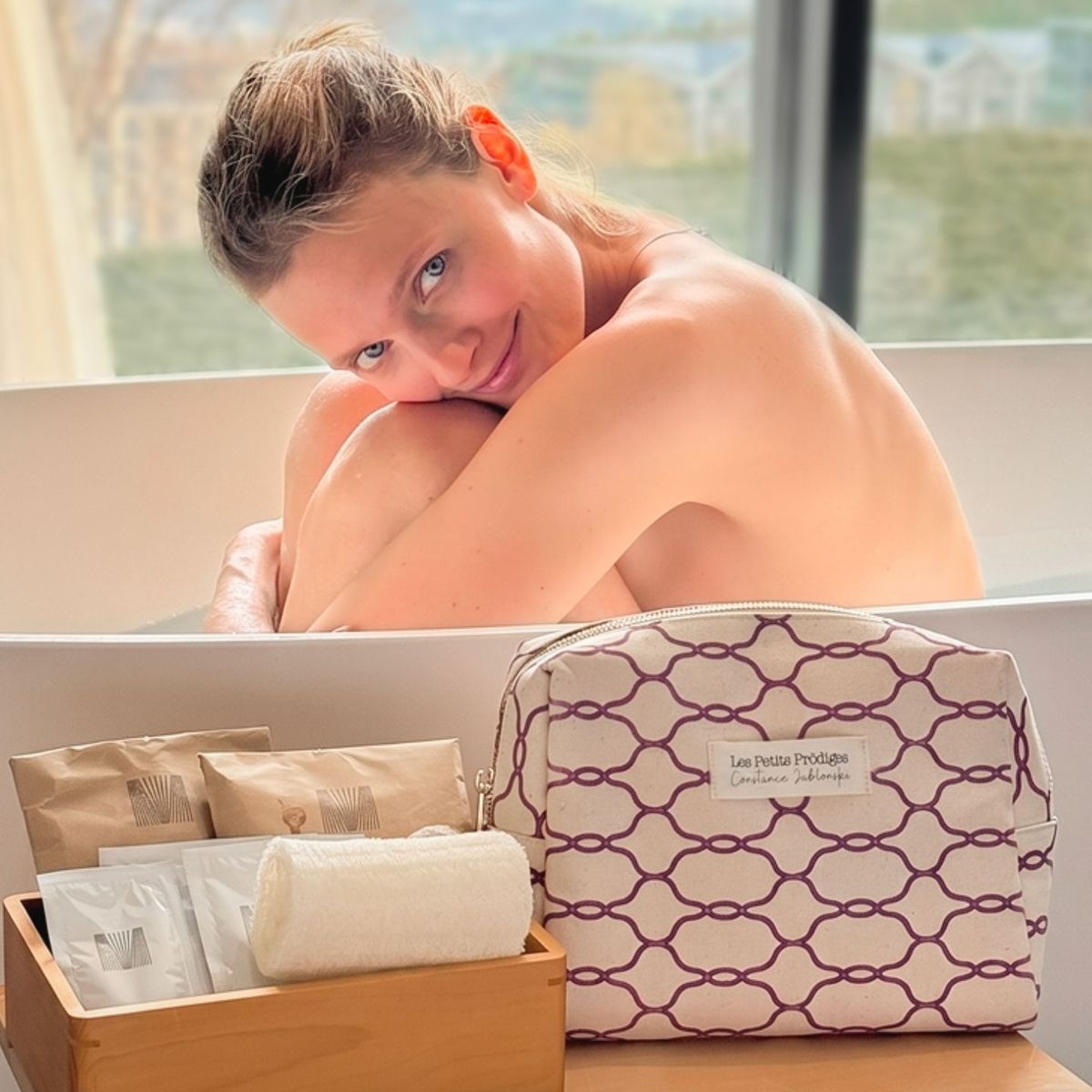 Femme souriante dans un bain avec la trousse d'été Les Petits Prödiges et ses soins