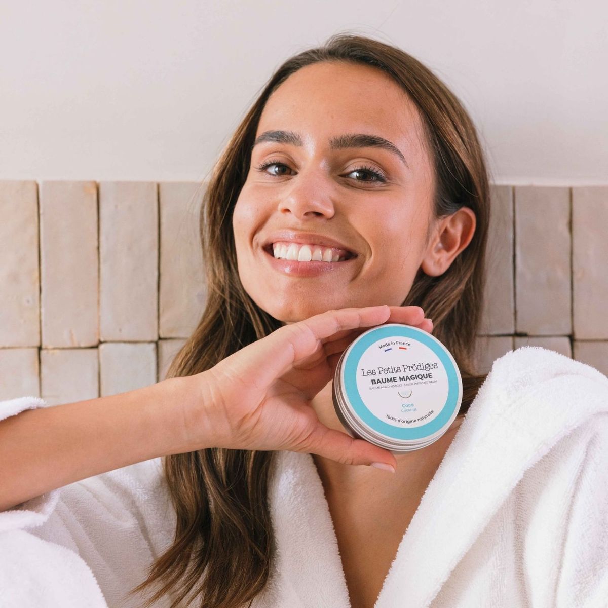 Femme souriante en peignoir tenant un pot de Baume Magique Coco