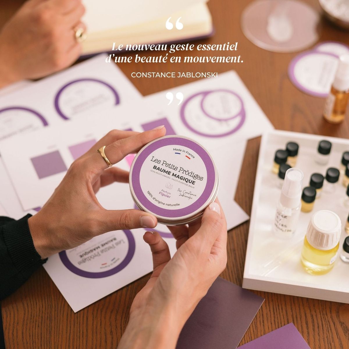Mains tenant un pot de Baume Magique Figuier au-dessus de flacons d'essences de parfum