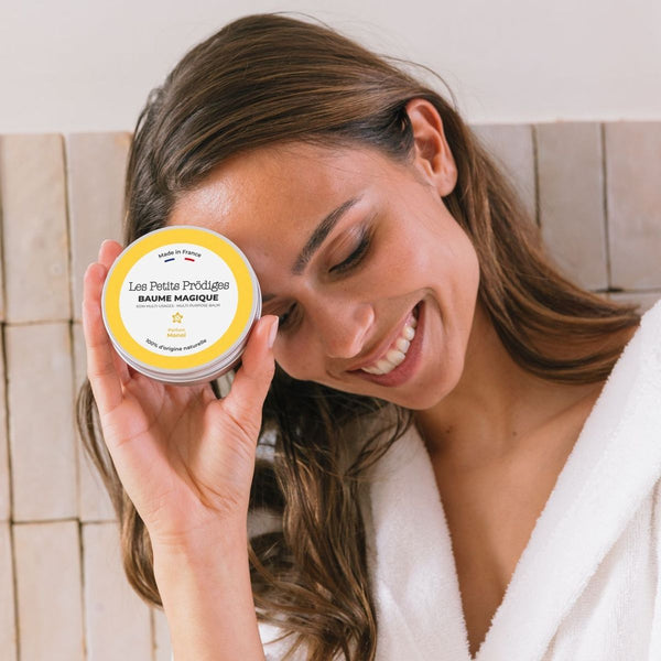 Femme souriante en peignoir tenant un pot de Baume Magique Monoï