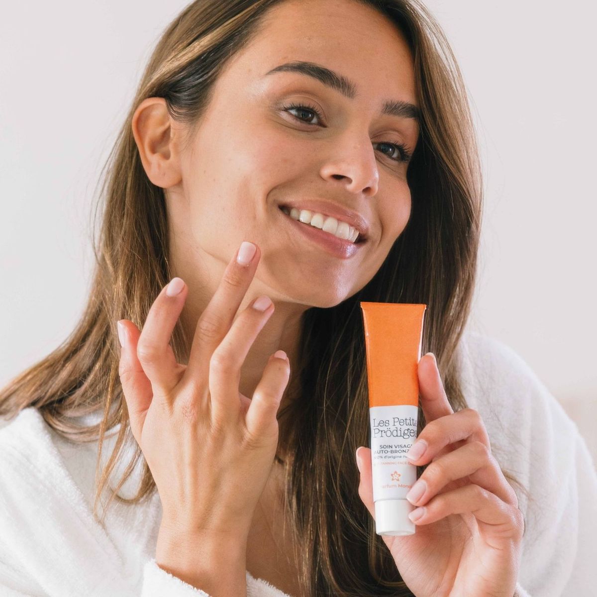Femme souriante en peignoir tenant le Soin Visage Auto-bronzant